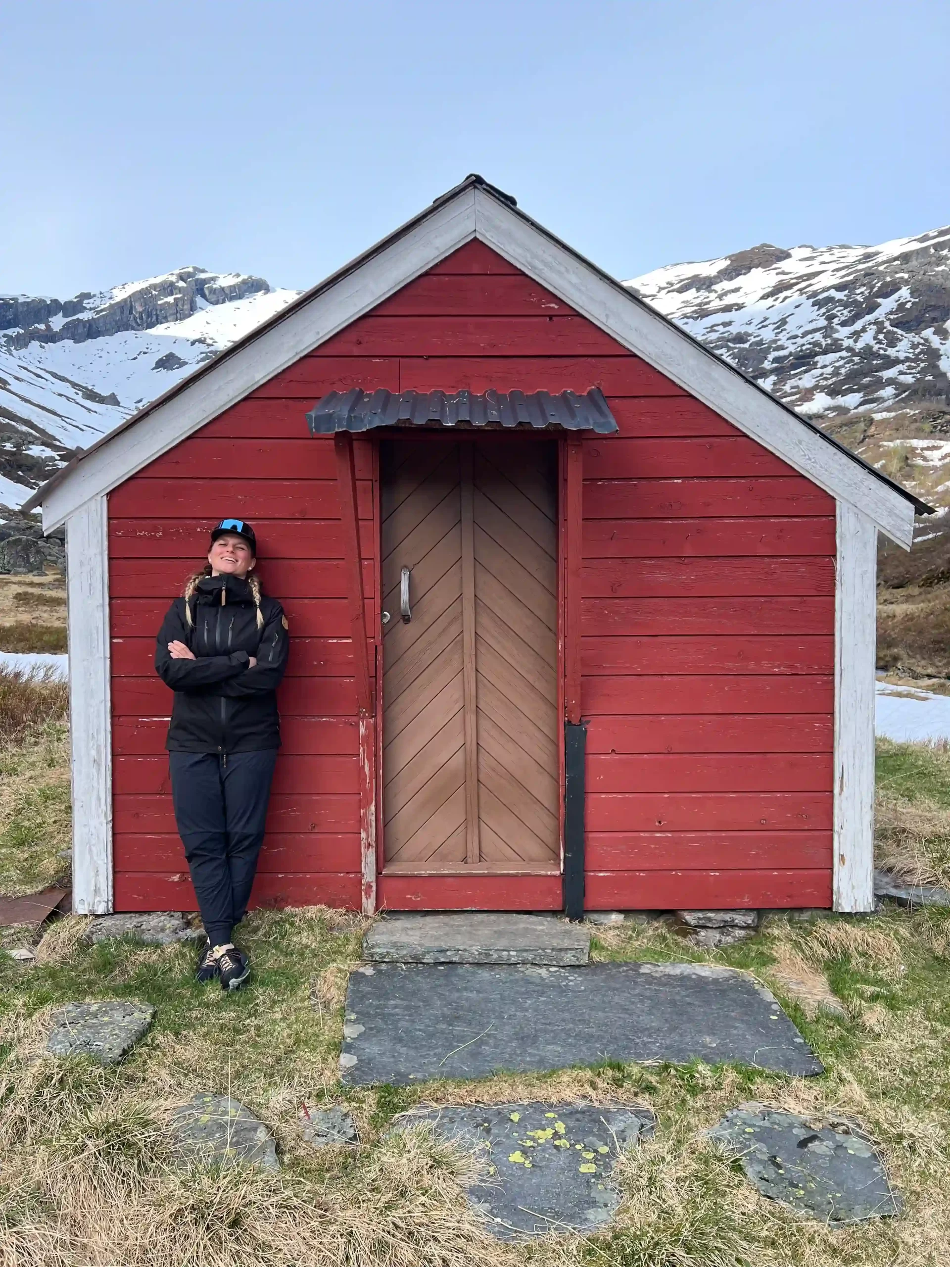 Jana standing by a red mountain cabin in Norway