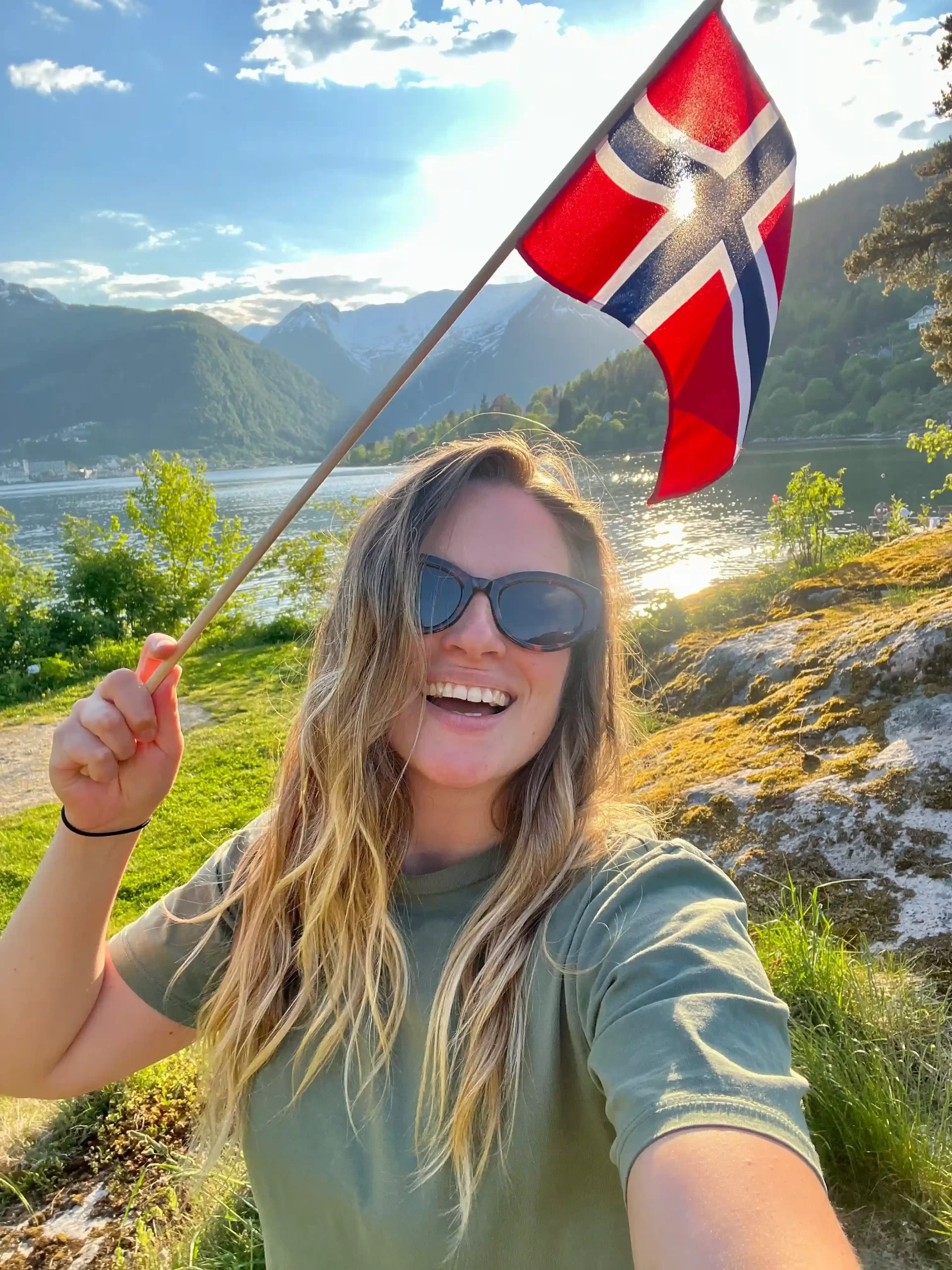 Jana holding a Norwegian flag by a fjord in Norway