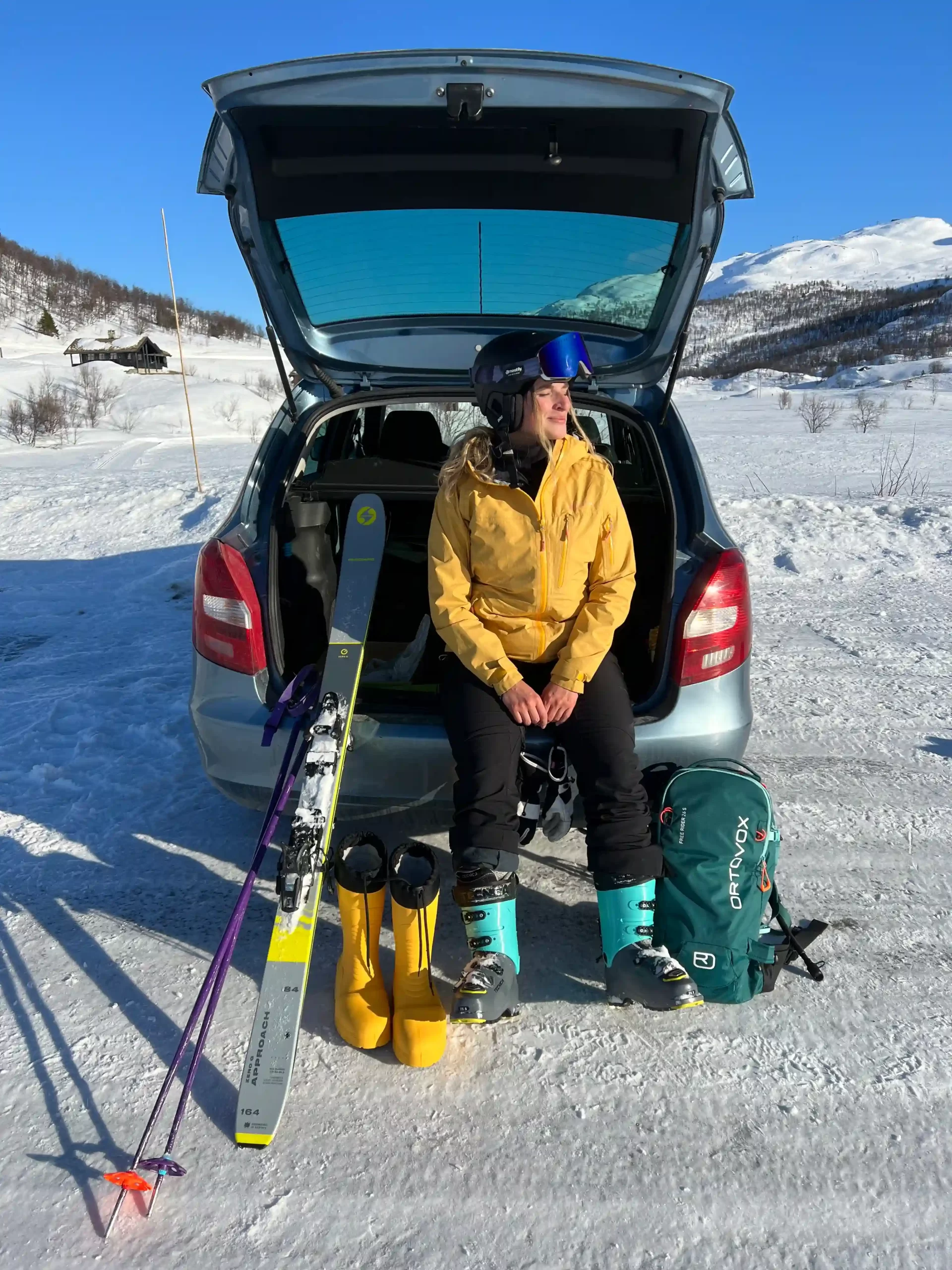About Jana sitting by her car with ski touring gear in snowy Norway