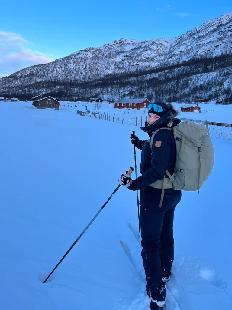 Consultations Woman skiing through snowy fields with mountains and farm houses in Norway