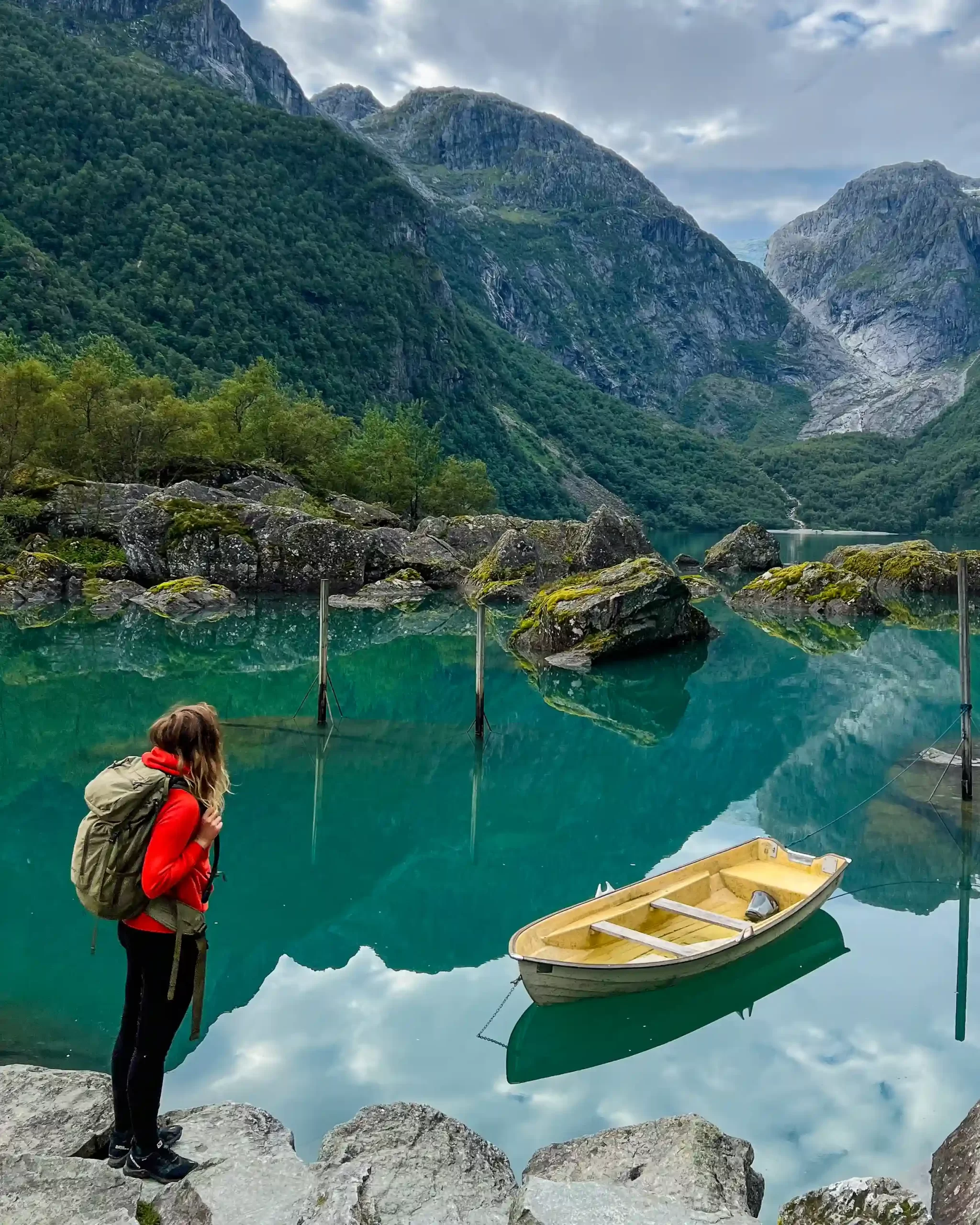 Woman with a backpack standing by a turquoise lake surrounded by steep mountains in Norway