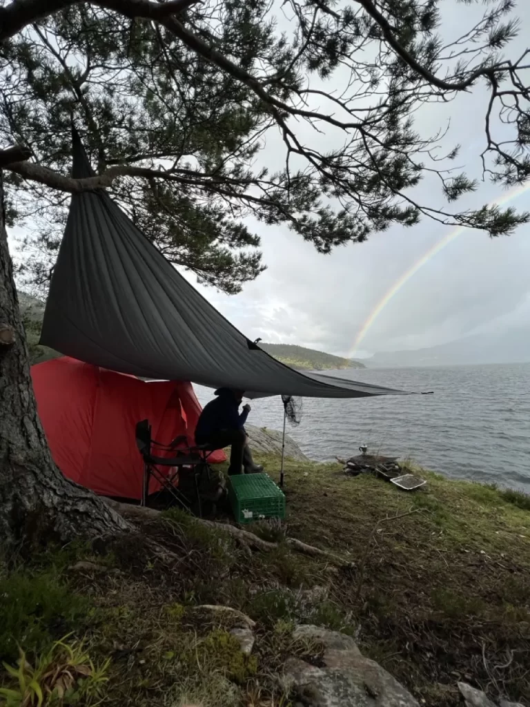 A tent and tarp pitched by a Norwegian fjord, showing wild camping on uncultivated land under the right to roam.