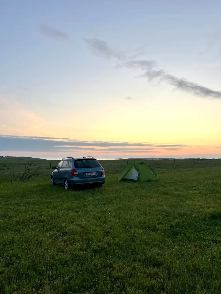 Car and green tent on a grassy campsite in Norway at sunset.