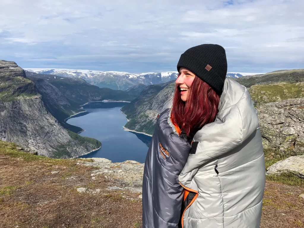 Hiker wrapped in a sleeping bag near Trolltunga with Ringedalsvatnet lake in the background.