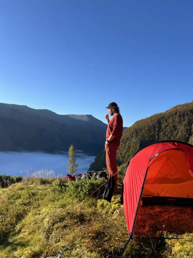 Red tent pitched above a Norwegian fjord with a person standing nearby.