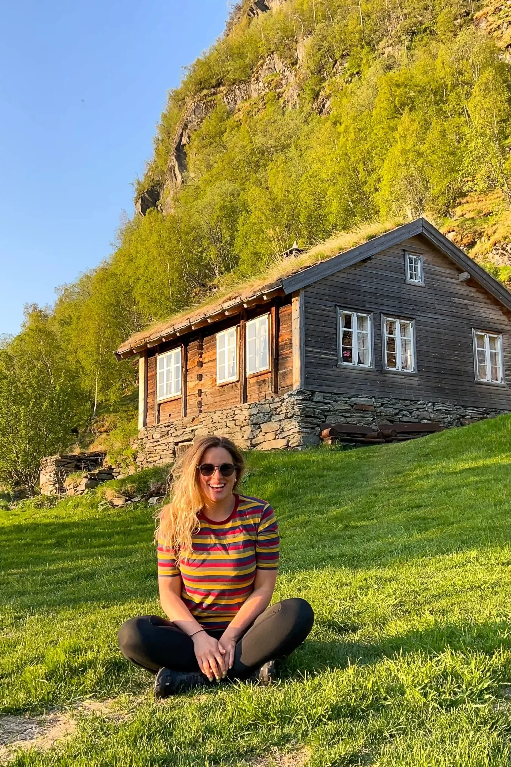 Woman sitting on grass in front of a traditional cabin in Norway